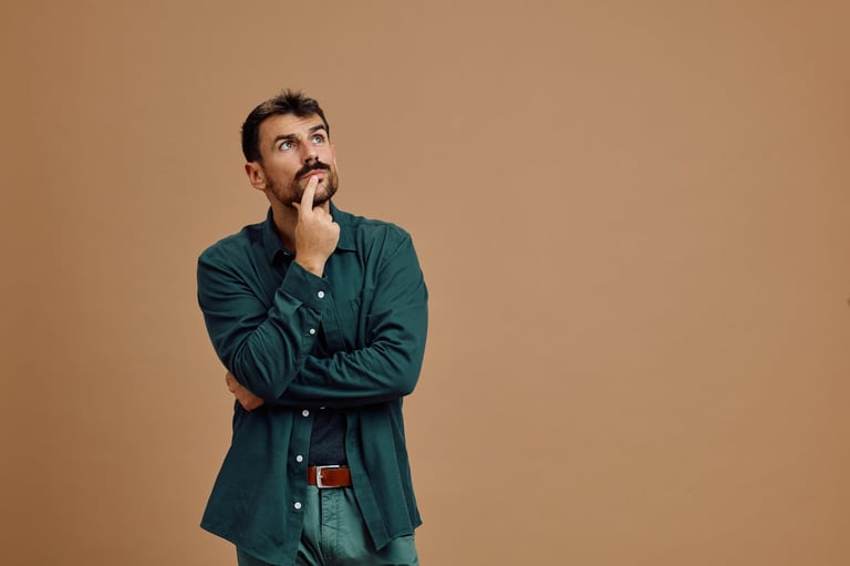 Man in teal jacket with hand to face looking upward in thoughtful pose against beige background