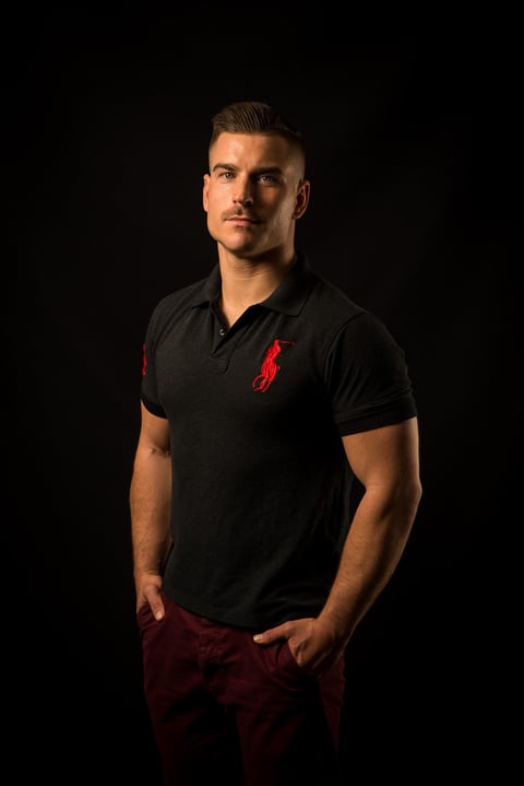 Coach Phill Terp - Man wearing black polo shirt with red emblem and burgundy pants standing against dark background in studio portrait