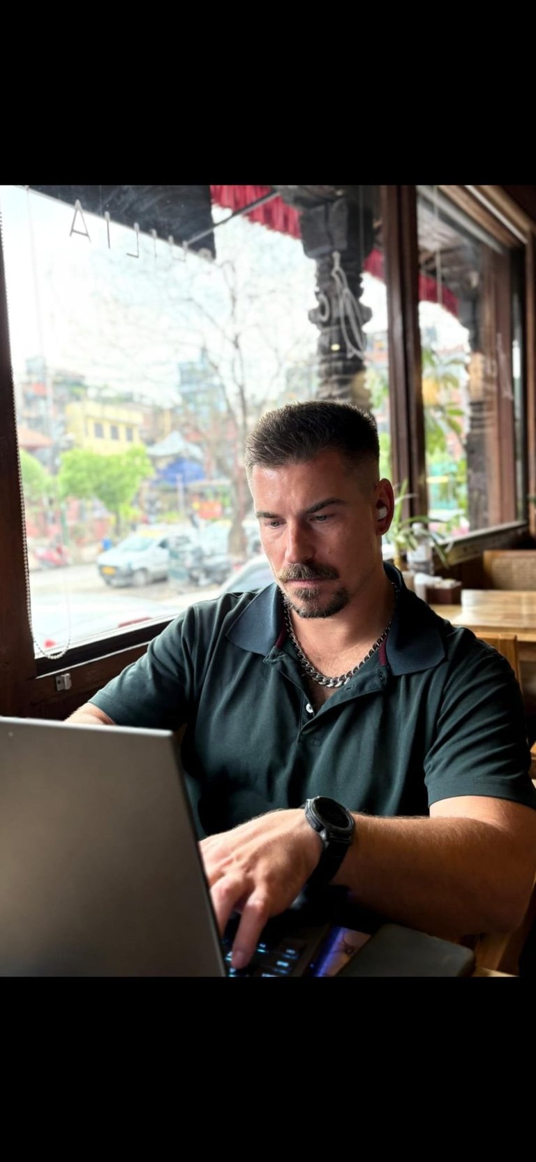 Man working on laptop in a cafe by window overlooking urban street with buildings
